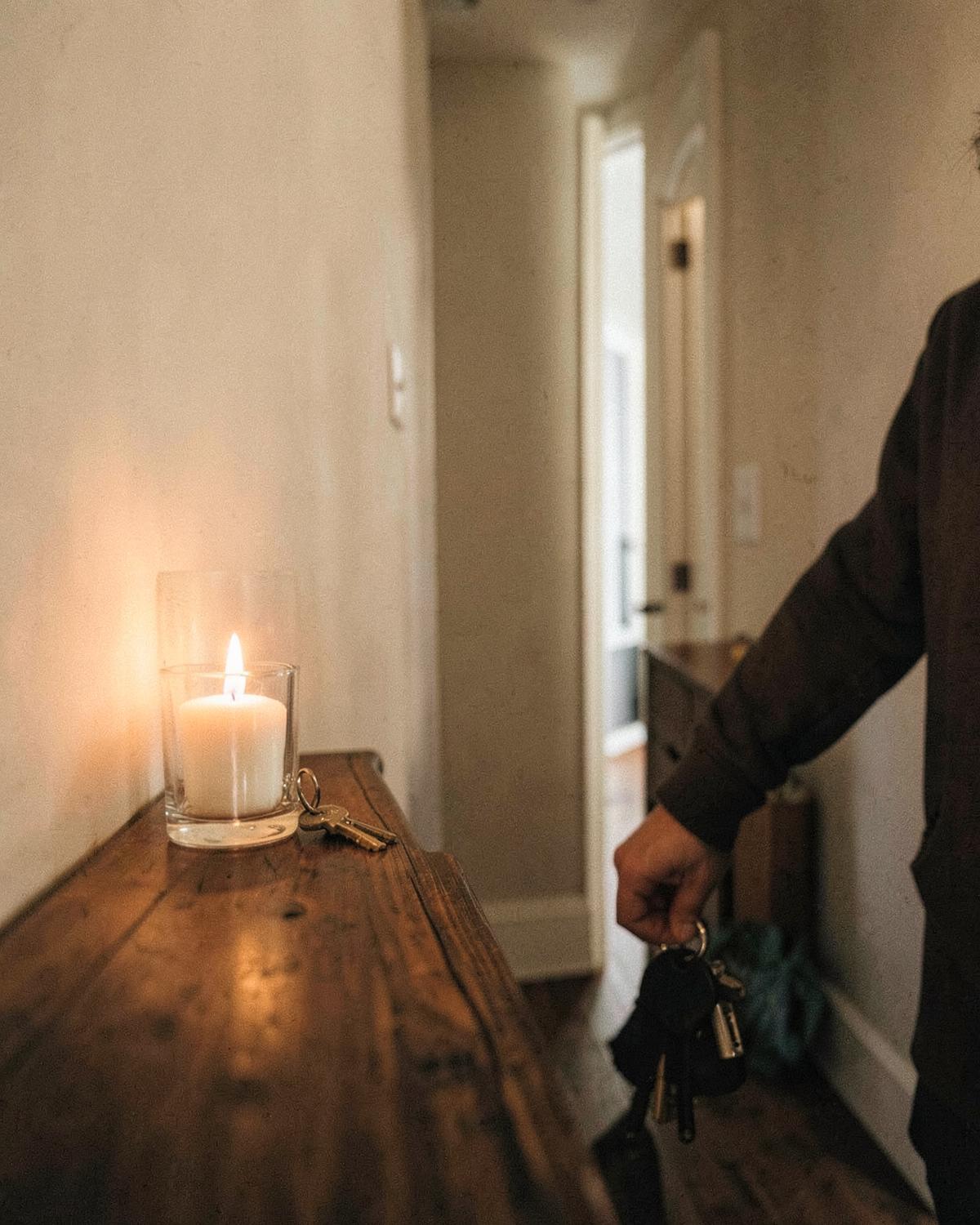 Pessoa chegando em casa e deixando as chaves ao lado de uma vela acesa