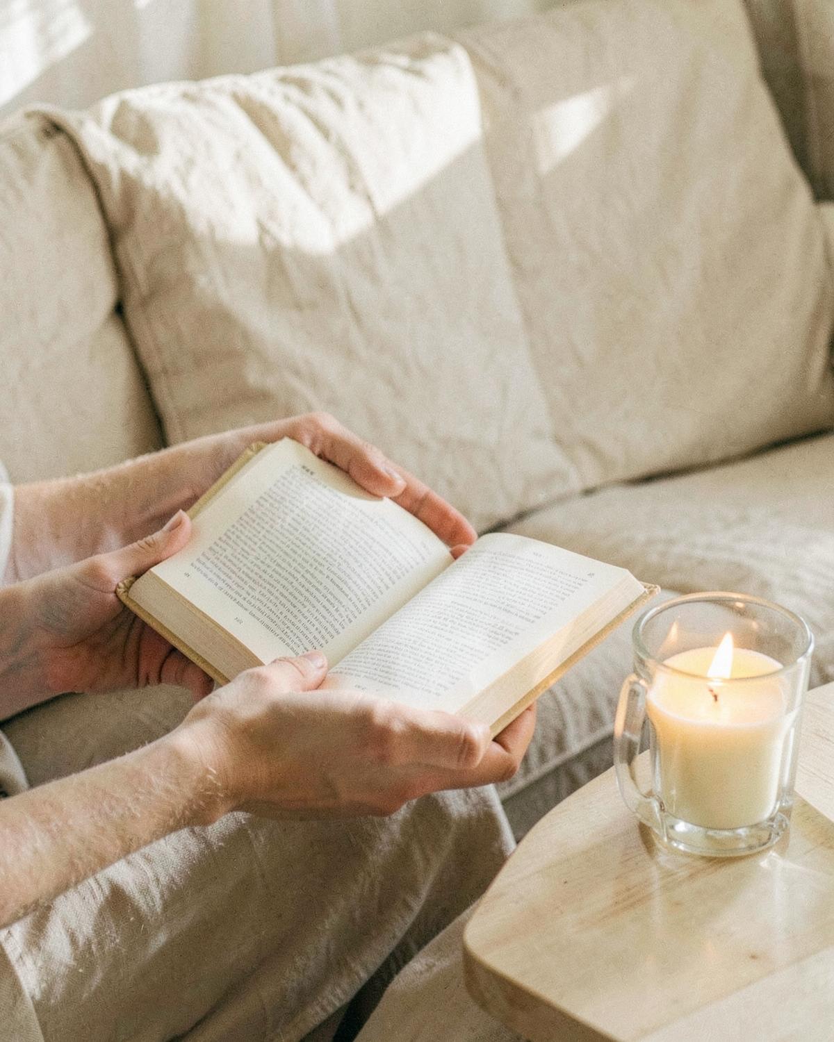 Mãos segurando um livro aberto ao lado de uma vela acesa